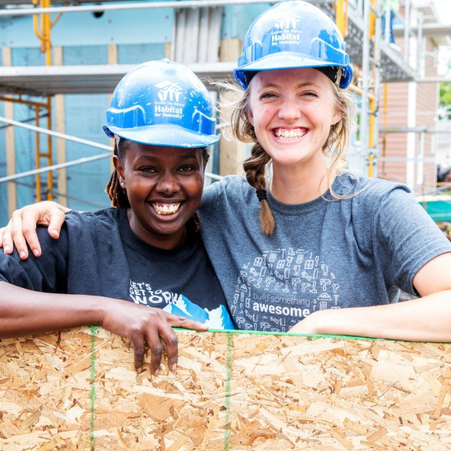 Two habitat for humanity volunteers smiling and posing together at a job site