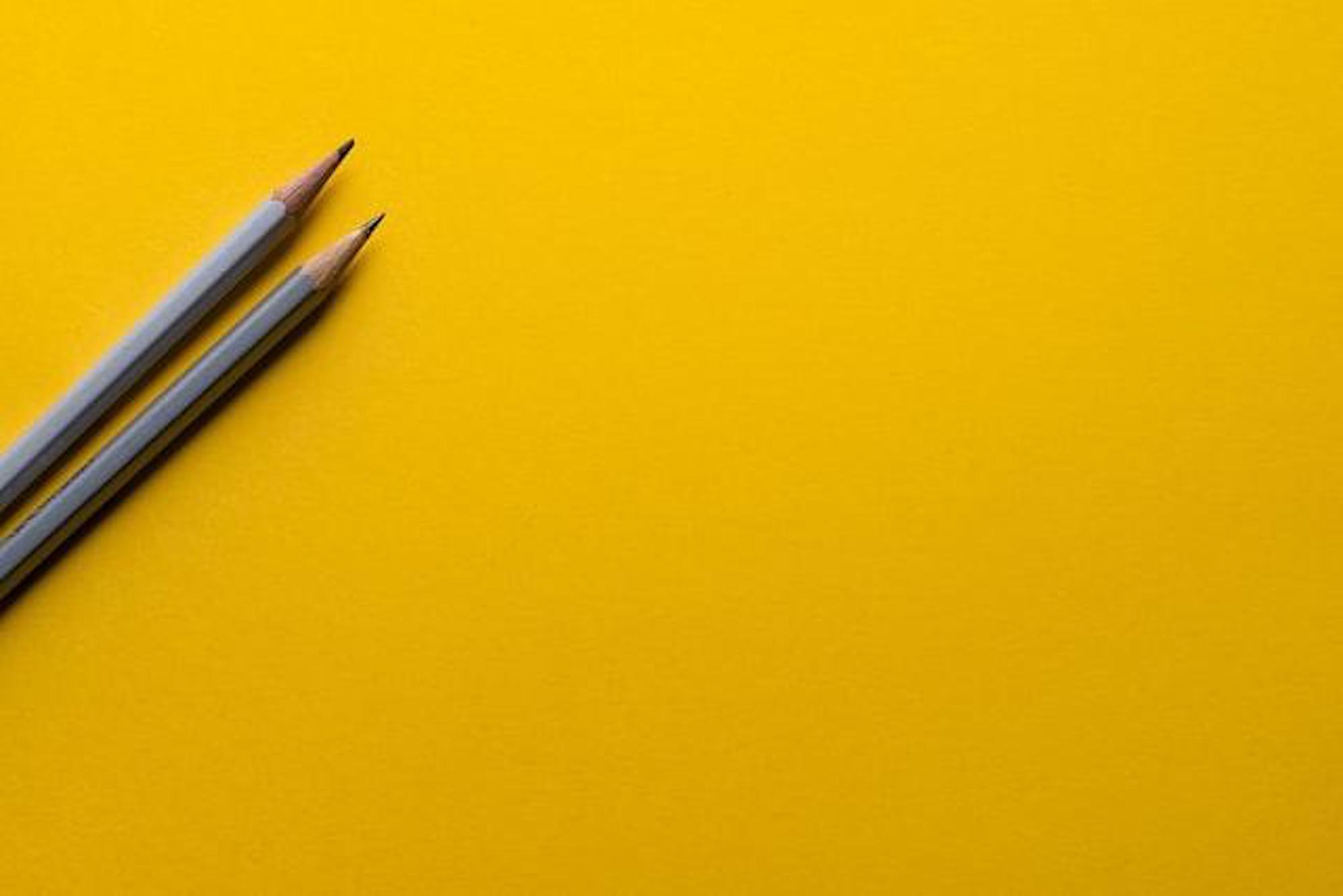 Two pencils on a yellow background. Always go with the simplest possible design.