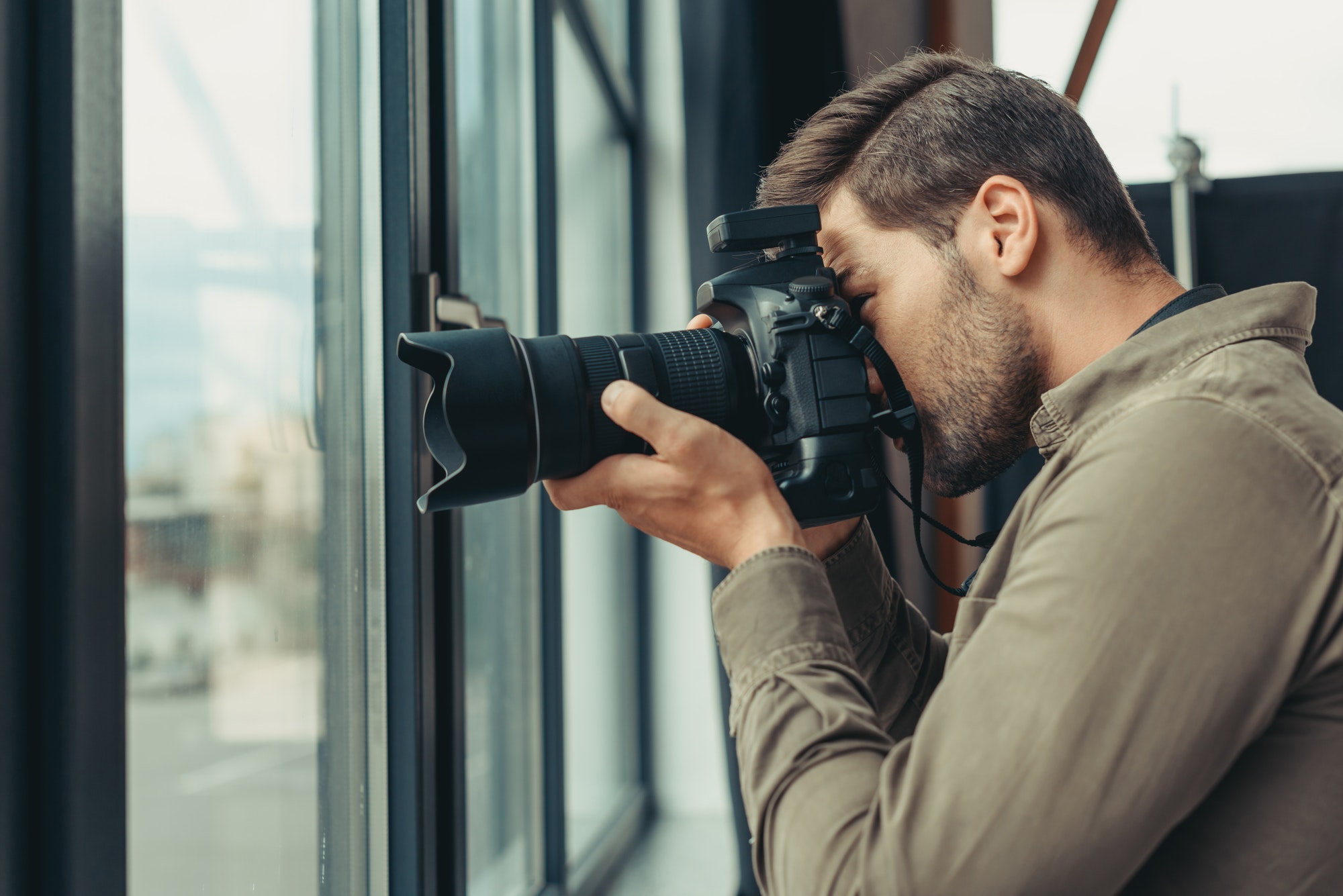 Professional male photographer with digital photo camera at window.