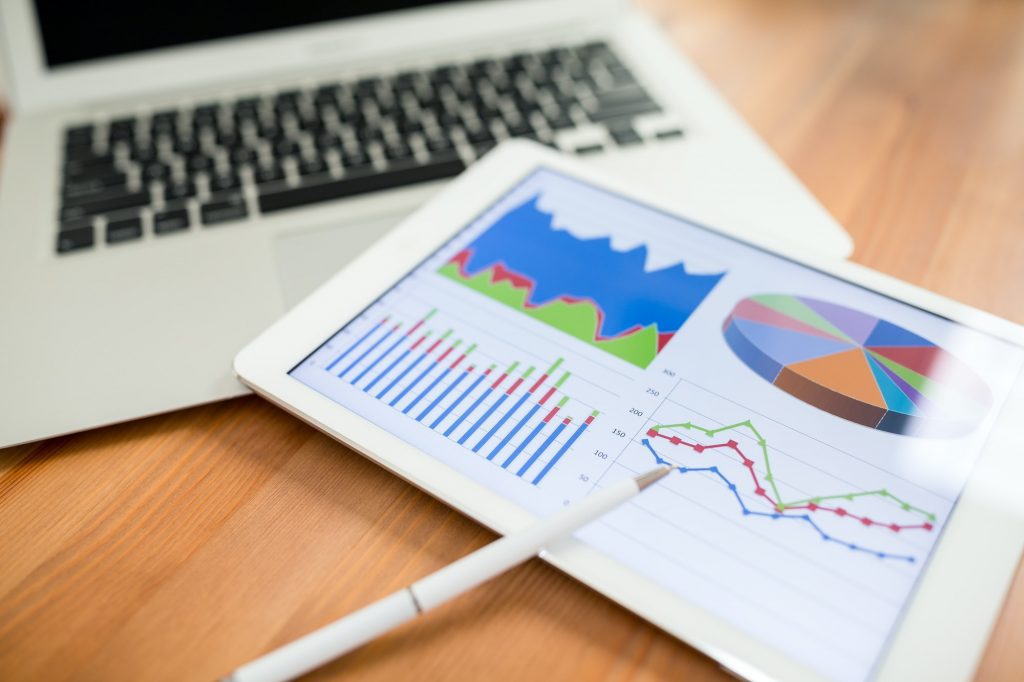 A laptop and tablet on a desk displaying data analytics.