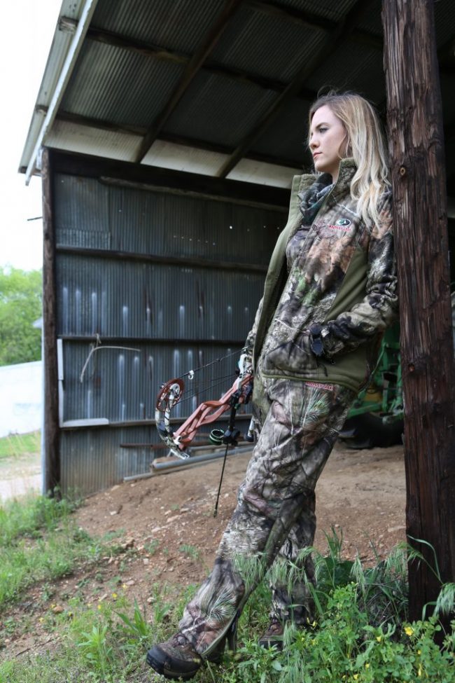 Female hunter in camouflage leaning on a wooden structure